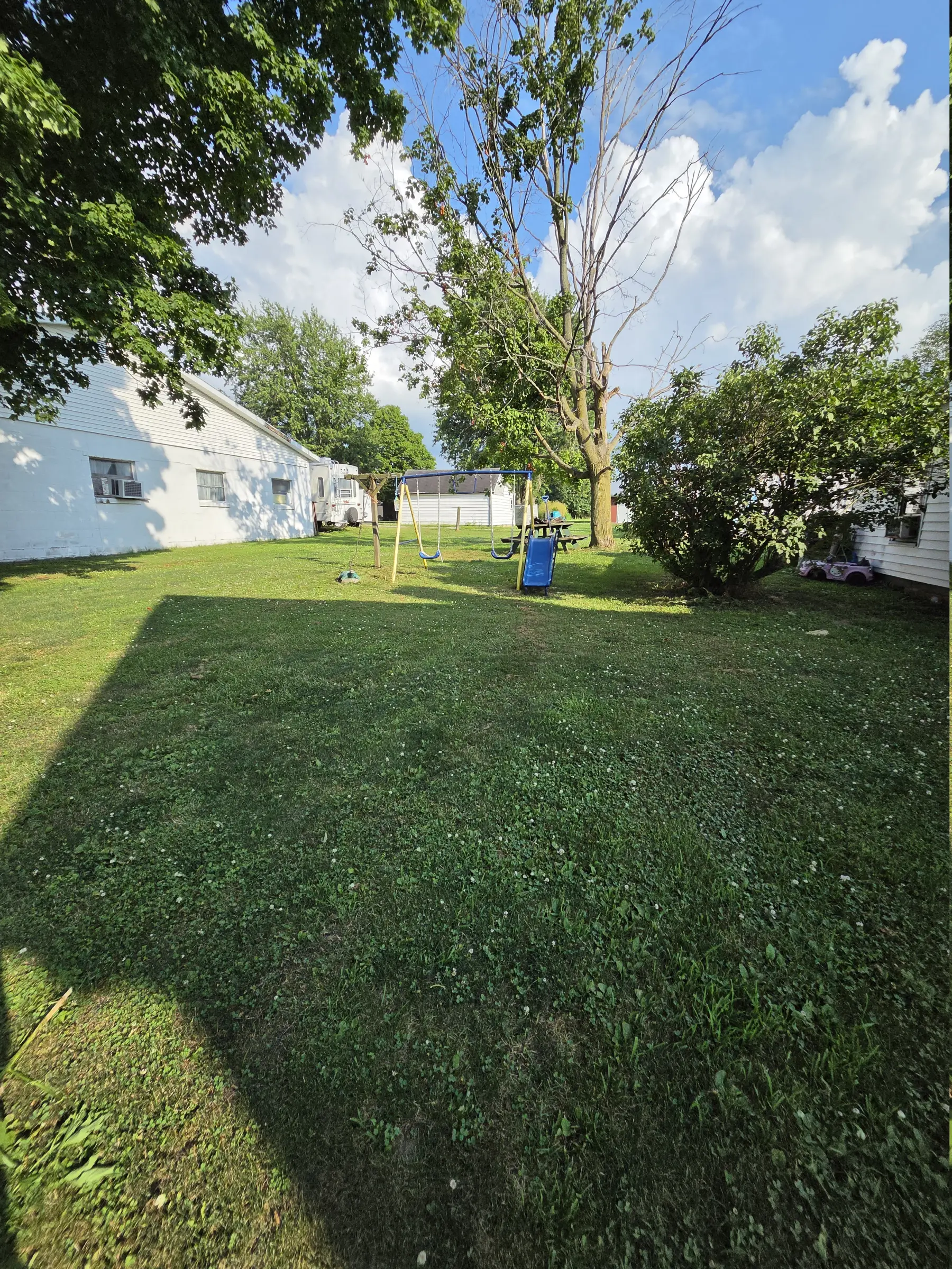 Maintained backyard lawn between homes with trees and a play set