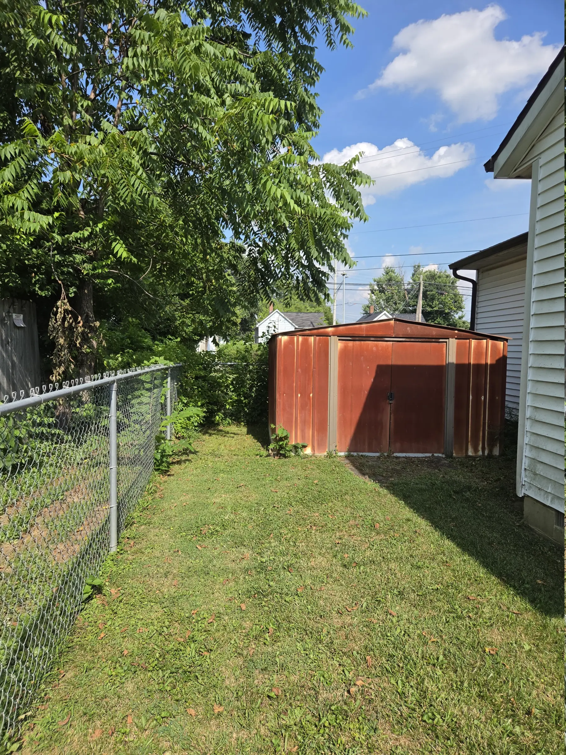 Maintained grass along a fenced side yard leading to a storage shed