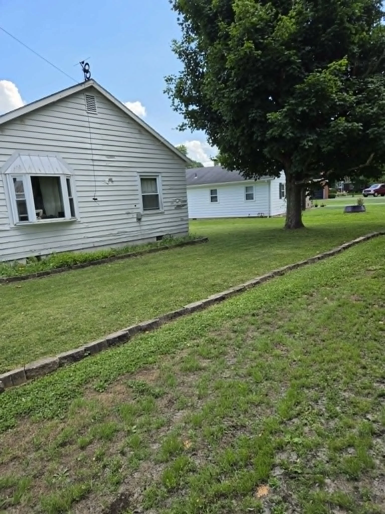 Maintained side lawn beside a white house and a large shade tree
